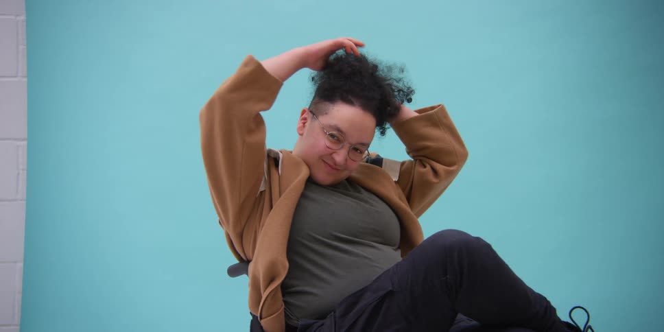 Model in a wheelchair smiling while modeling in a blue background studio