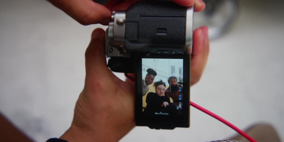 A person holds a camera while watching video footage of three people on it
