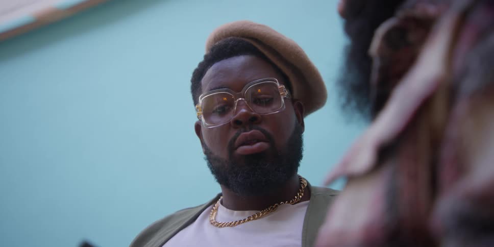 A person in a gold chain and a hat standing in front of a light blue wall