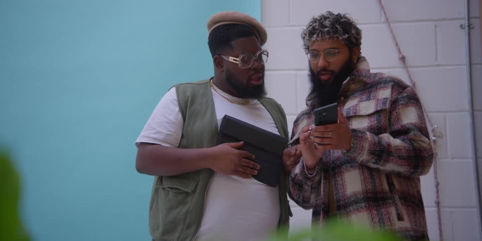 Two men talk and look at their devices