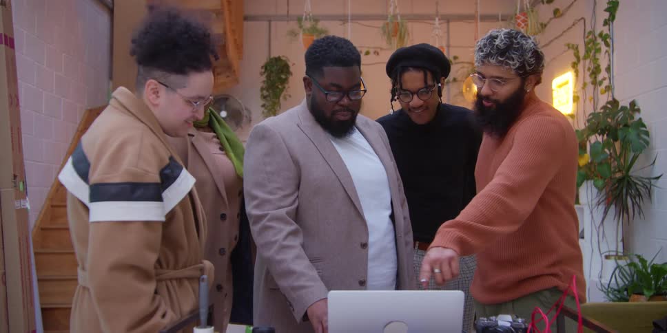 Coworkers discuss content displayed on laptop sitting on table near camera