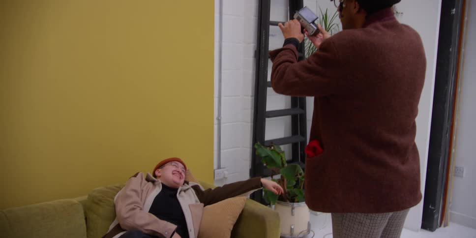 A man is taking pictures with a camera of a man sitting on a couch