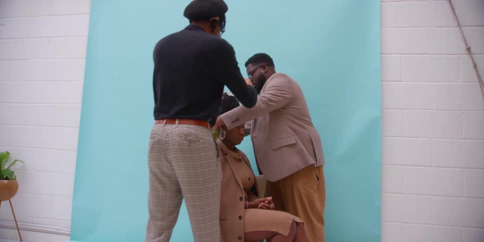 Two men placing a scarf on a model woman who is sitting in a studio