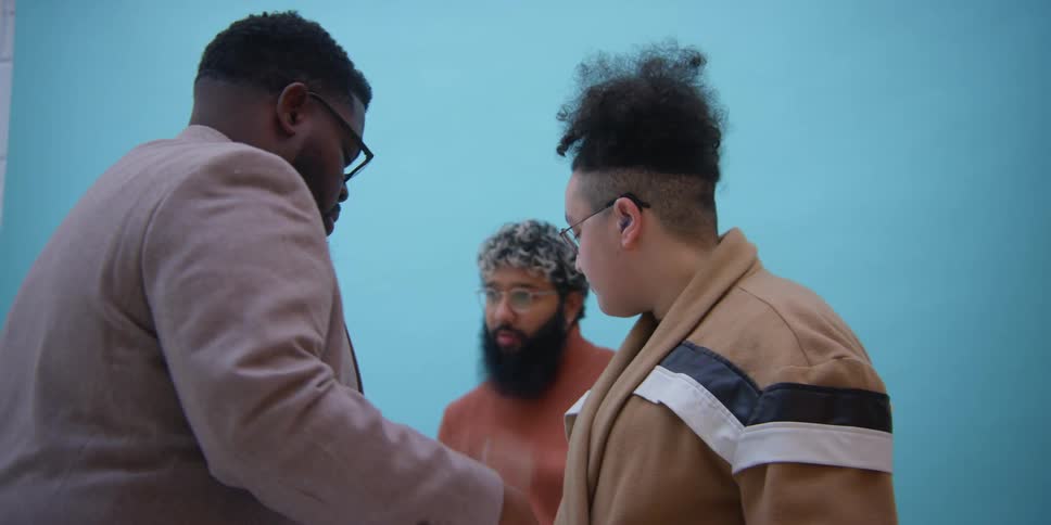 A black man is dressing up another man as one stand to watch