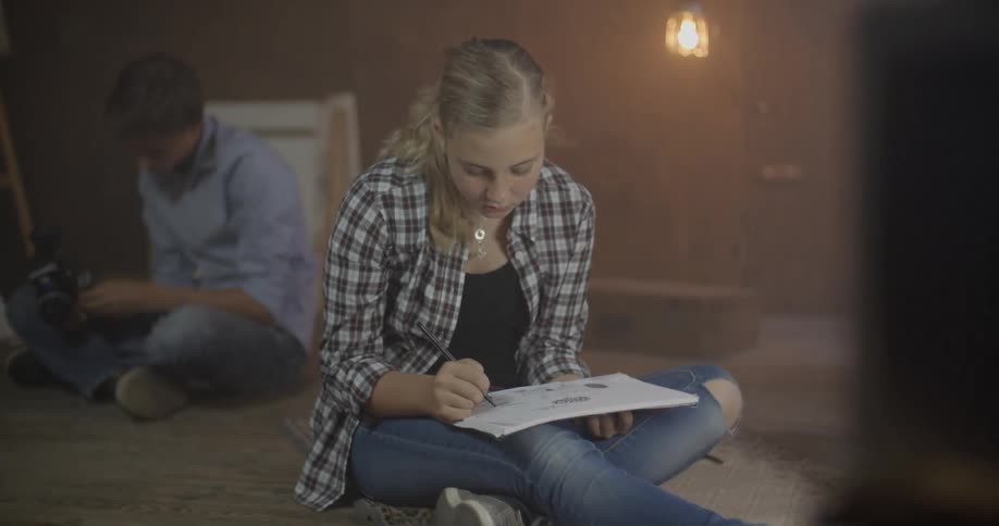 A young girl sits on the floor writing in a notebook