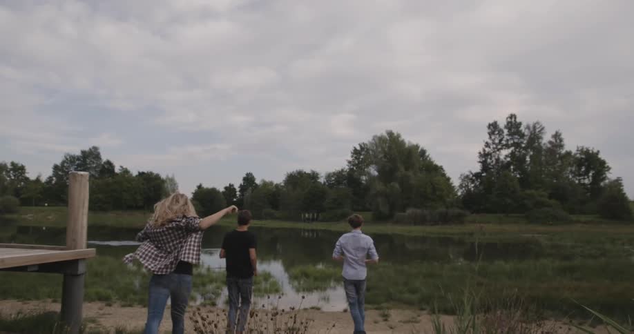 Two boys and girl running toward small pond on cloudy day
