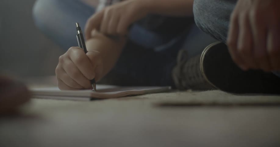 Person sitting cross legged on the floor writing in a notebook