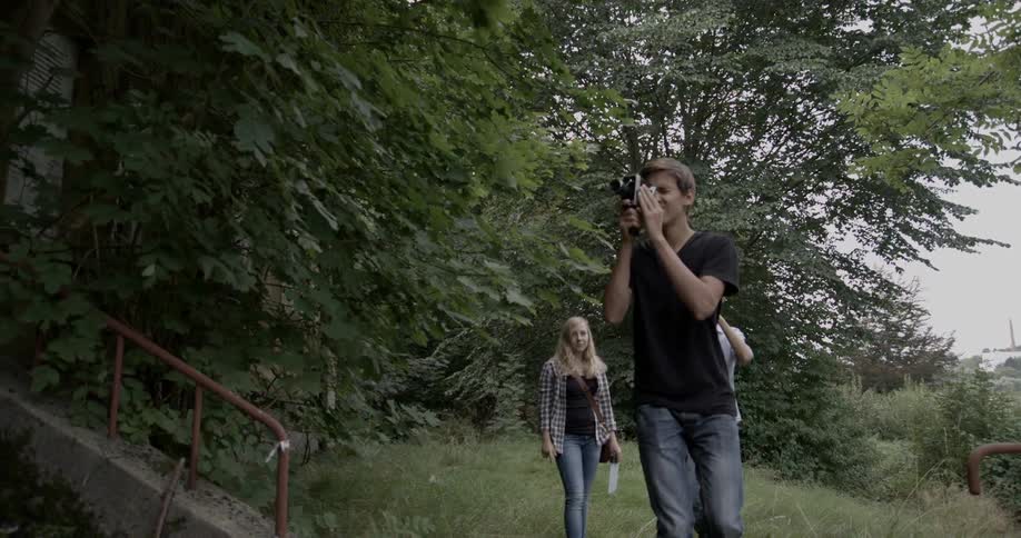 A young man films outdoors with two other young people