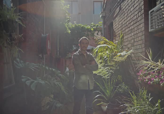 Man with arms crossed in the middle of a corridor between houses with garden