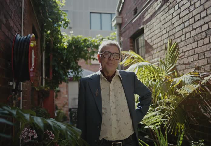 A man with a slight smile stands in an alley full of plants