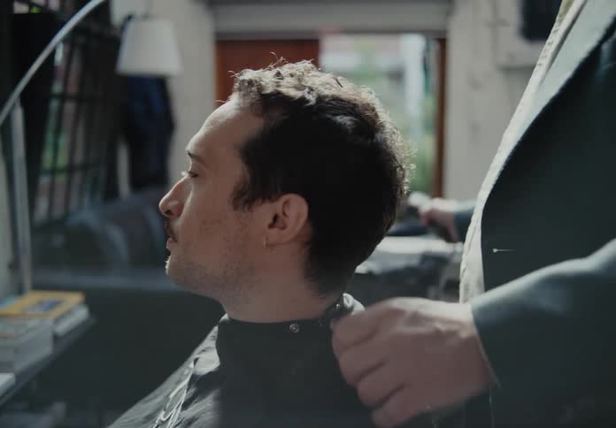 A man sits in a chair as a barber prepares him for a haircut