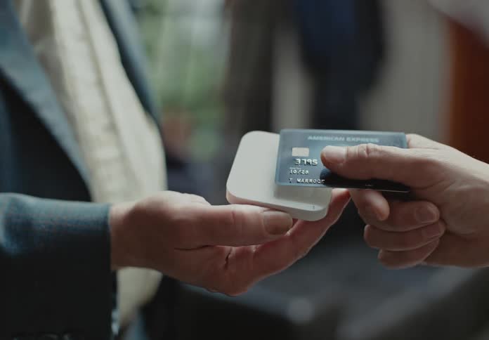 A man holds a small scanner for another man to scan a credit card