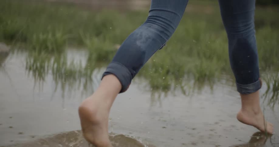 A person wearing rolled up jeans runs through a grassy puddle