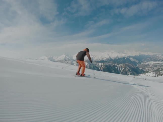 A skier is swiftly descending a slope with snowcapped mountains in the background