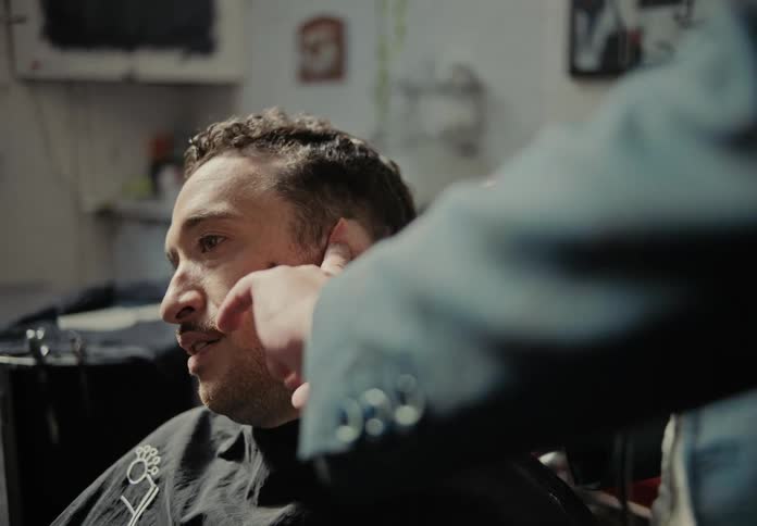 A person is getting a haircut in a salon with the focus on the hands of the stylist using clippers