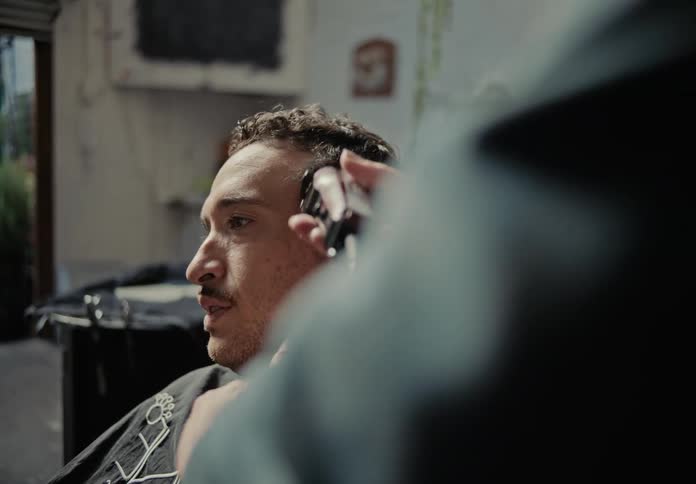 Man sitting in barbershop chair talks while barber trims his hair with clippers