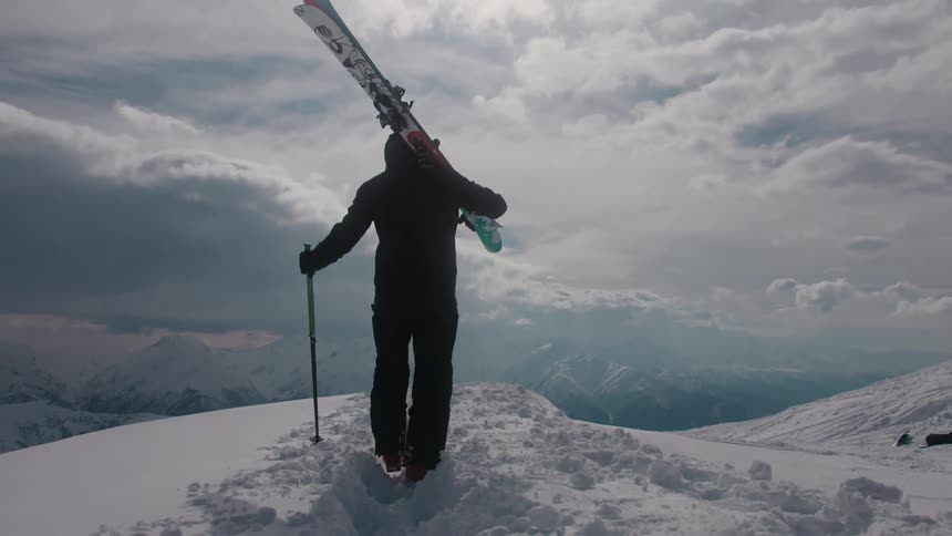 A person walking on a snowy mountain carrying a ski