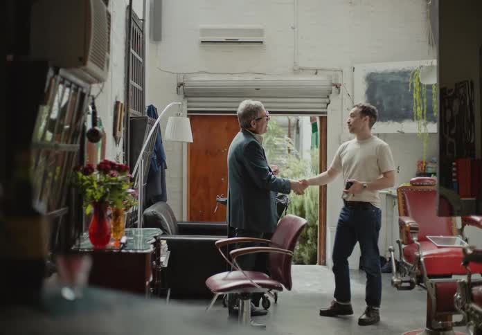 A barber and client shake hands and talk in a barbershop
