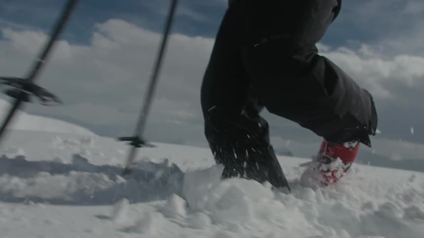 A person walking in the snow with a ski on his shoulders