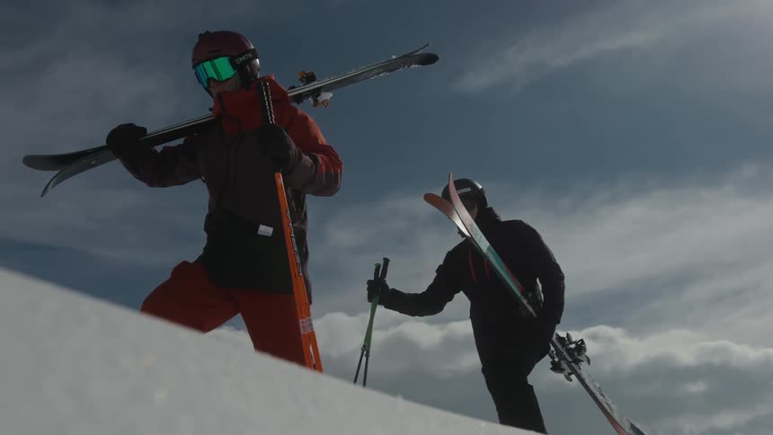 Two skiers climbing a snowy hill holding their skis