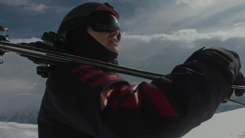 A person wearing goggles and a helmet has ski on his shoulder and is looking at the environment around him