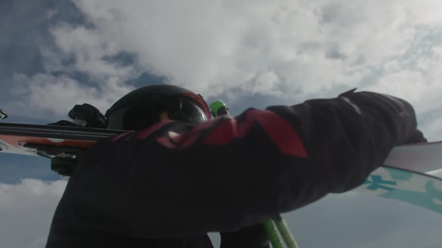 A person in dark clothing holding skis and wearing a helmet stand in a snowy slope