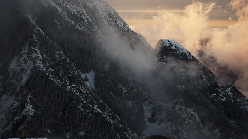 Landscape of a mountain with forest and snow and haze of clouds passing around