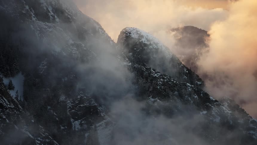 Rugged mountain peaks enveloped in mist and illuminated by the golden hue of the sunset