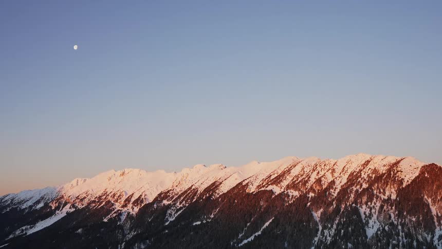 Snowcapped mountains with the moon in a clear blue sky