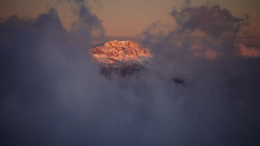 Landscape of a mountain covered in snow with clouds passing around in slow motion