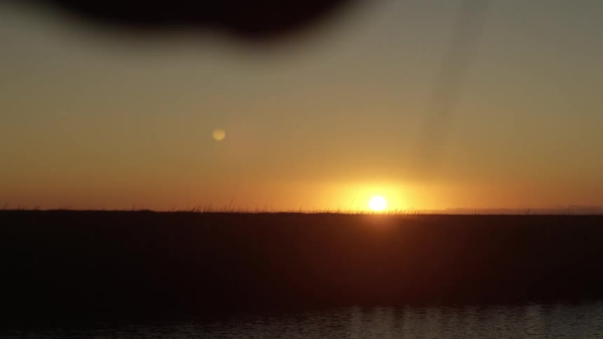 Silhouette of a mans arm fishing in the middle of a river with the sunrise on the horizon