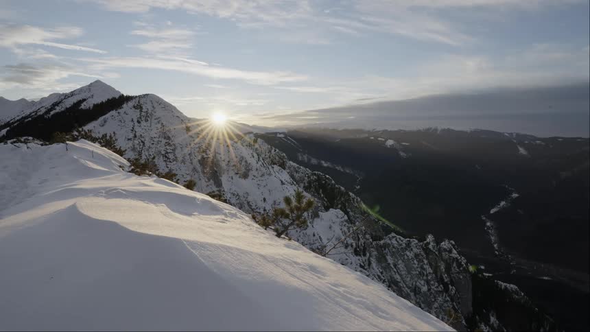 The sun peaks over snow covered mountains