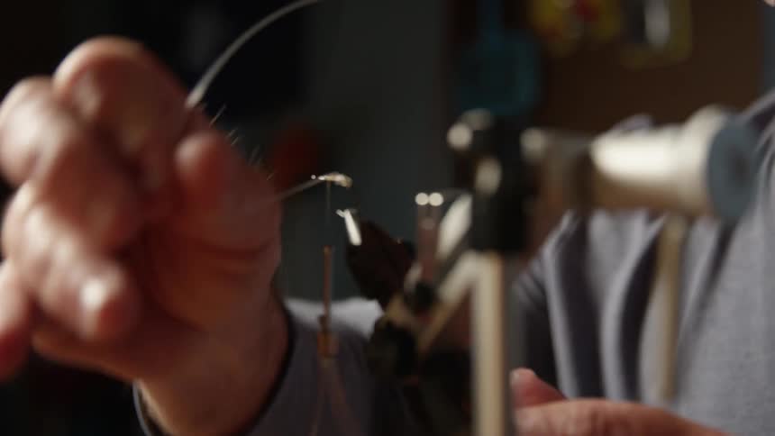 A man is concentrated while passing a thread over a very small object that is attached to a support