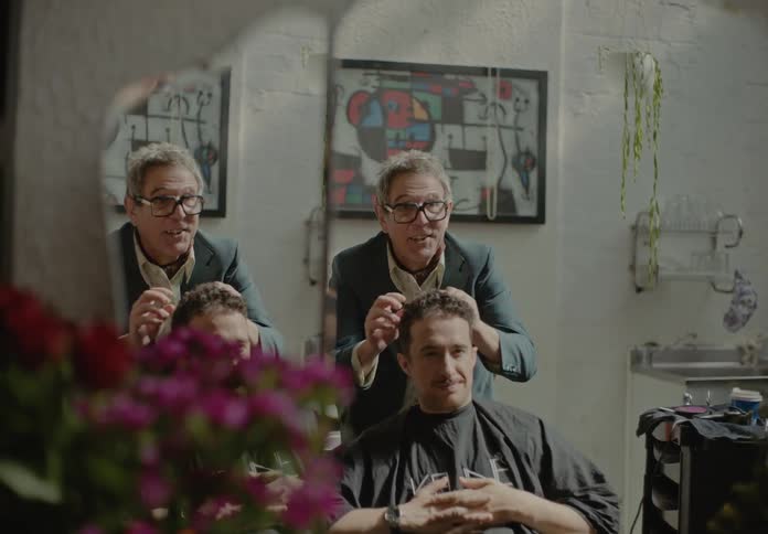 Elderly barber arranging and showing a clients hair style indoors at a barber shop