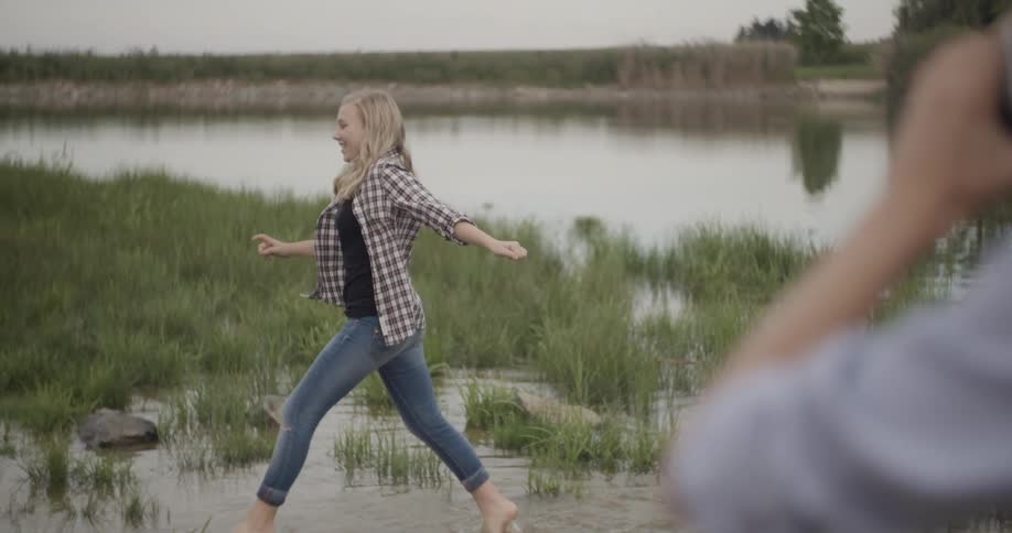 A woman laughs running through water and kicks water towards a young man