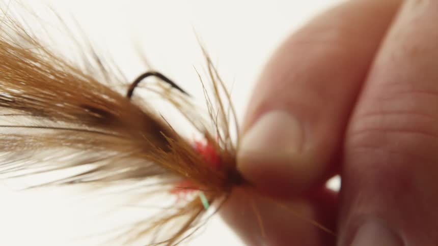 Male hand holding a fishing bait with feathers and hook outdoors during day time