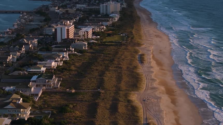 An area with many residences and buildings facing a beach with sea waves crashing on the shore