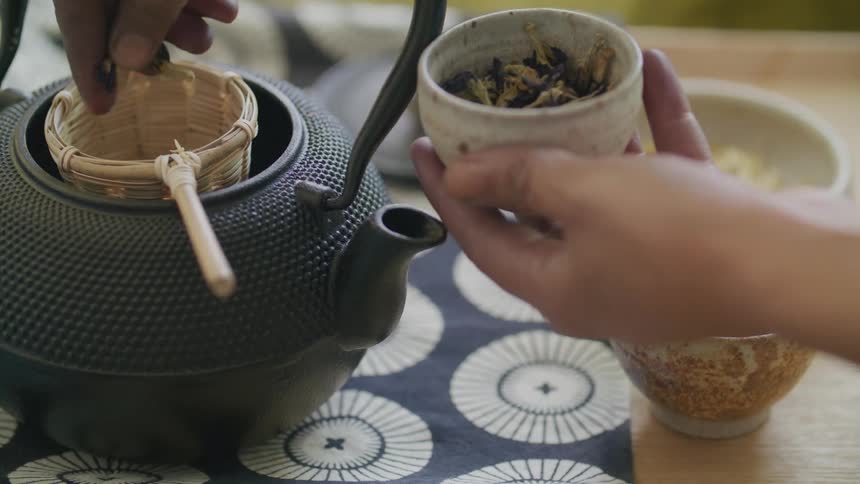 Closeup of a womans hands preparing tea by putting herbs in the kettle