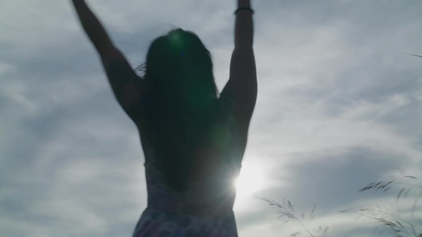 A woman in a dress is posing and raising her arms up