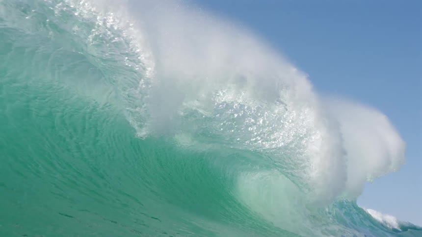 Huge turquoise blue wave breaking into the sea in slow motion