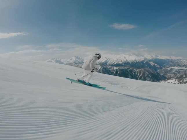 A person in white clothes is skiing down a mountain and on the horizon to a region with many other stone mountains