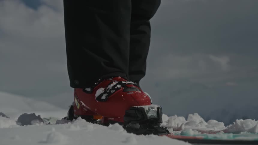 A person with red boots connects them to a ski that is in the snow