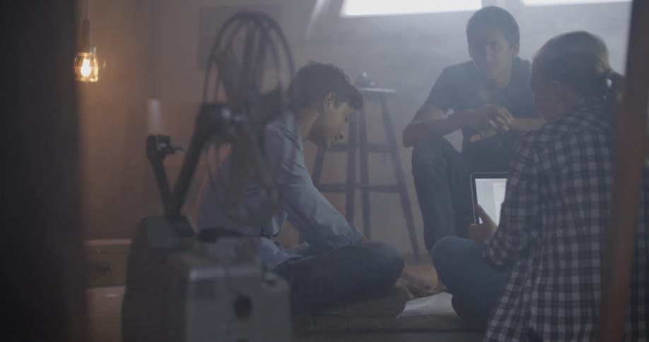 Three people sit in a hazy room with a projector on the floor