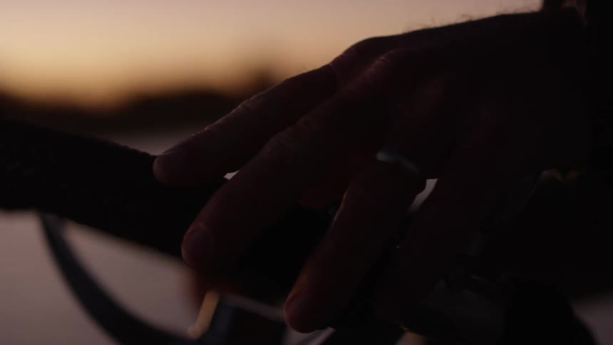 Closeup on the hand of a man piloting a small boat on a river in a dawn sky