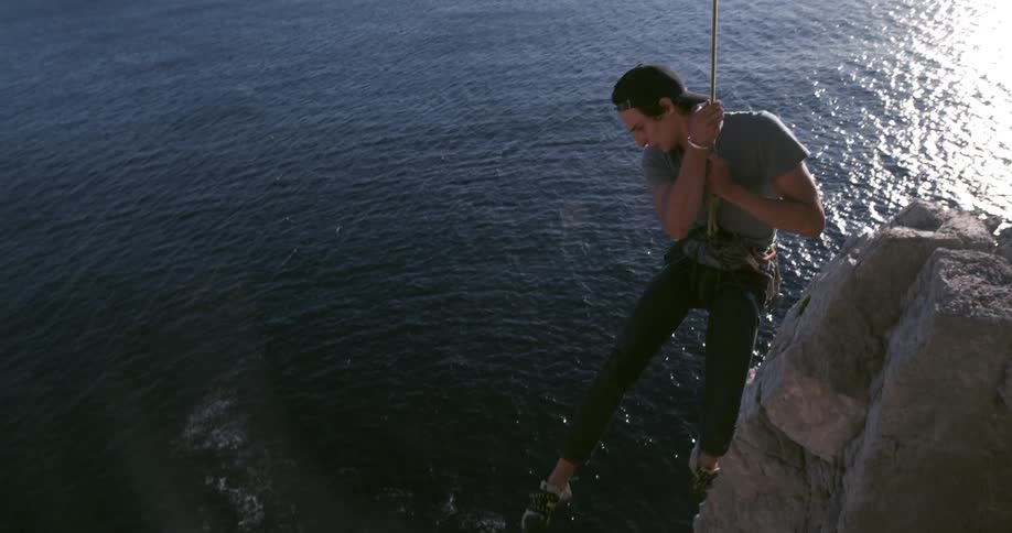 A man hanging from a rope climbing a mountain on the sea coast