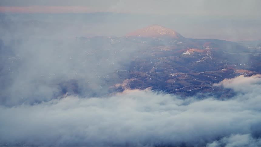 An aerial view above the clouds and on the ground there is a large mountain