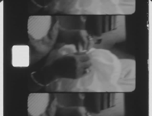 Shaky footage of a woman repairing a dress caught on vintage film