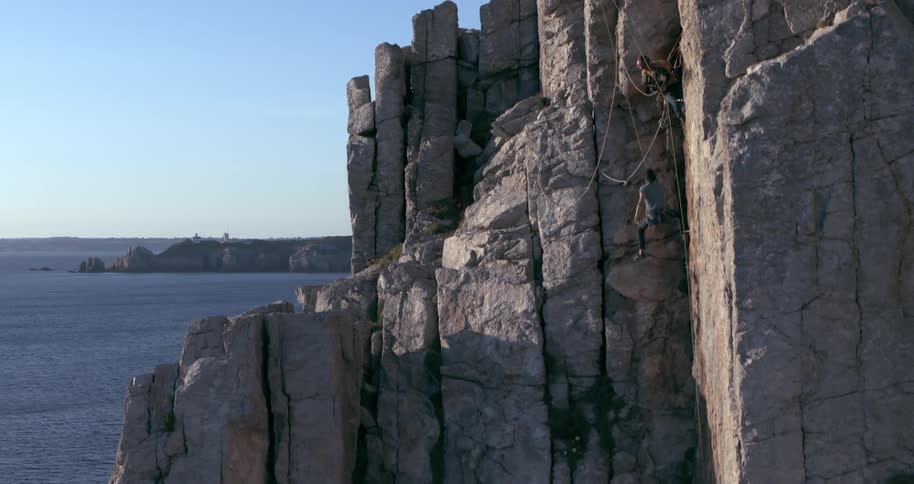 Male rock climber slips on seaside cliff and falls to dangle on safety line under female climber