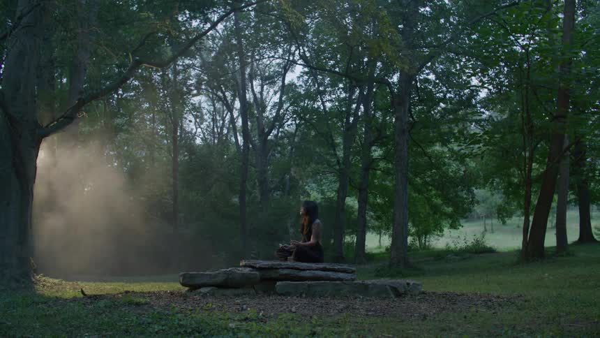 A woman sitting on a rock smoking in the forest