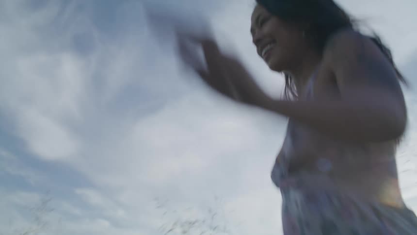 A woman in a dress is walking in a field with tall grass and starts running and is happy
